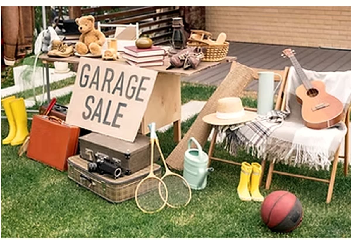 Household goods, instruments and furniture laid out at a garage sale on a lawn.