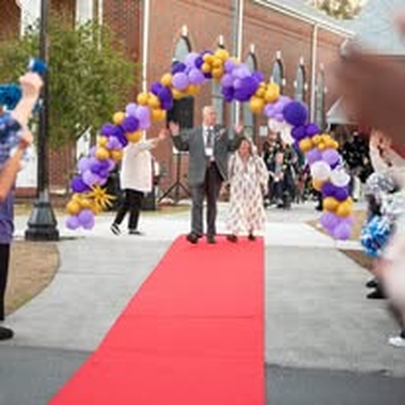 A man in a suit and hat walking the red carpet with a companion.
