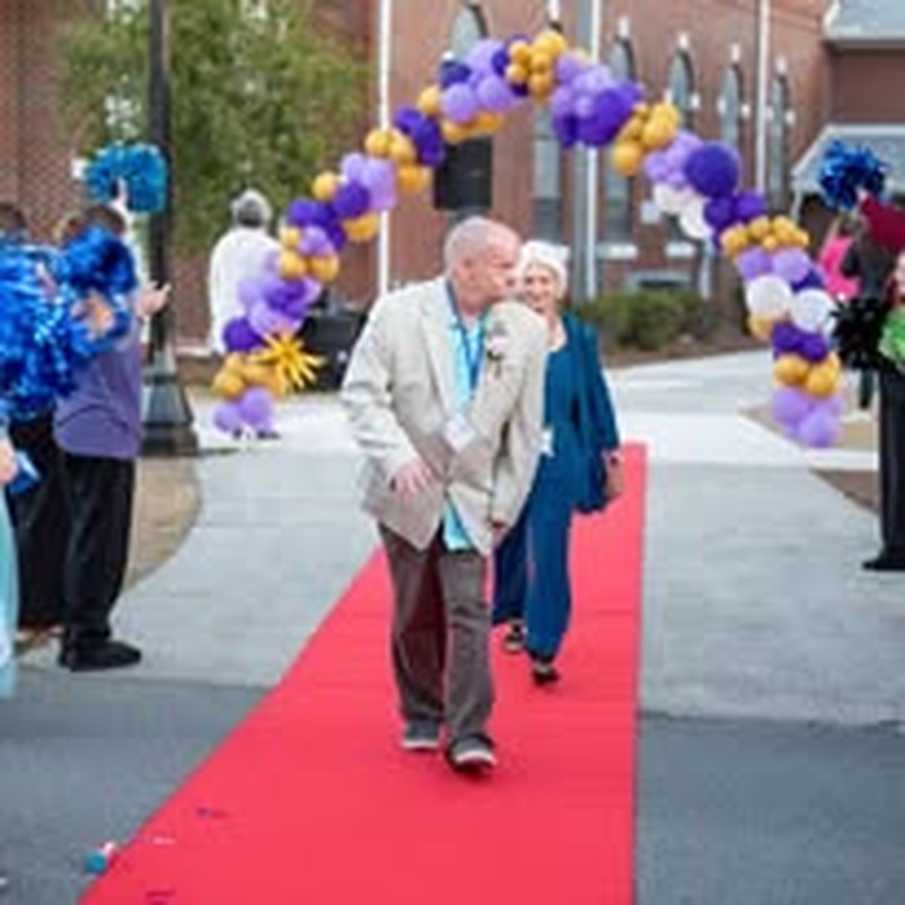 An individual making a grand entrance at the gala with cheering volunteers.